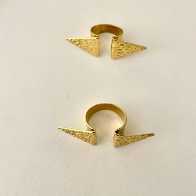 Dois anéis dourados abertos com pontas triangulares texturizadas sobre superfície branca
