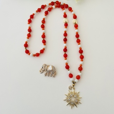 Colar com contas vermelhas e pendente estrela dourado ao lado de broche elefante dourado