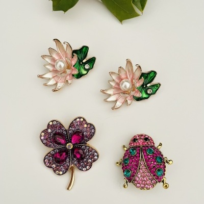 Quatro broches decorativos coloridos com flores, trevo e joaninha sobre fundo branco com folhas e bagas vermelhas