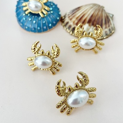Broches de caranguejo dourados com pérola, junto a conchas marinhas azul e bege