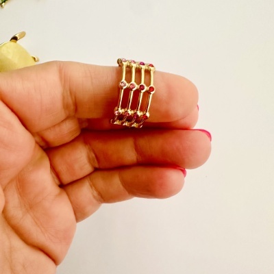 Anel dourado com pedras vermelhas na mão sobre fundo branco