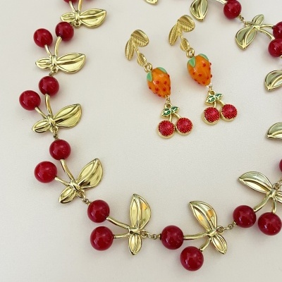 Conjunto de colar e brincos com design de frutos coloridos sobre fundo branco.