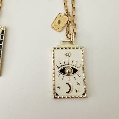 Colar dourado com pendente retangular decorativo e símbolo de olho, lua e estrelas.