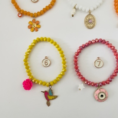 Quatro pulseiras coloridas com pendentes distintos e etiquetas numeradas, organizadas sobre fundo branco.