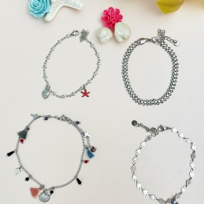 Quatro pulseiras prateadas com pendentes variados sobre fundo branco com flores e uma estrela-do-mar decorativa.