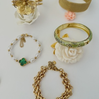 Pulseiras douradas com detalhes em pérolas e motivos florais sobre fundo branco