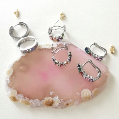 Brincos variados em metal com pedras coloridas sobre uma placa de ágata rosa.