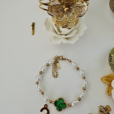 Pulseira com flor verde e contas brancas e douradas, bracelete dourada com flor metálica, números dourados 1 e 3 em fundo branco.