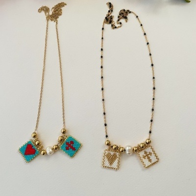 Duas pulseiras douradas com pendentes quadrados em contas e detalhes de pérolas artificiais, sobre fundo branco e flores coloridas