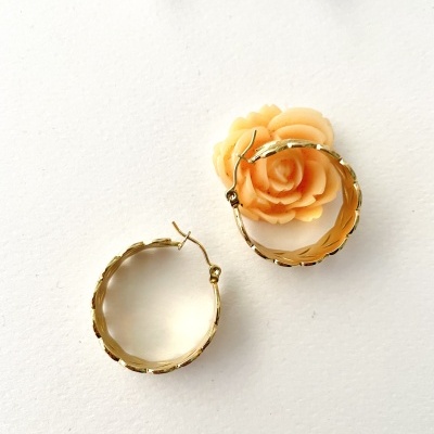 Brincos de argola dourados com textura ondulada junto a uma flor pêssego