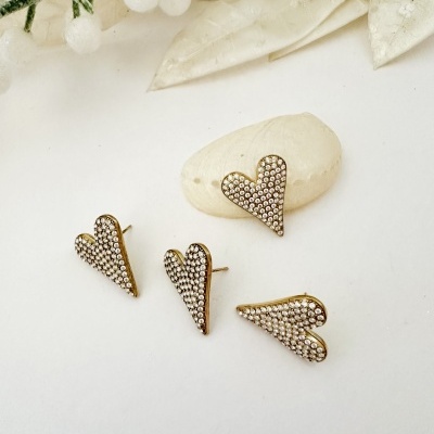 Brincos em forma de coração dourados com cristais sobre superfície branca