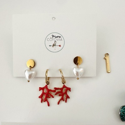 Brincos com pedras brancas em forma de coração e coral vermelho pendurados em cartão branco.