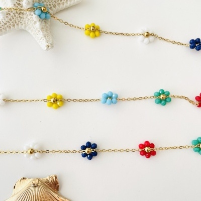 Colares dourados com pingentes de flores coloridas sobre fundo branco com concha e estrela do mar.