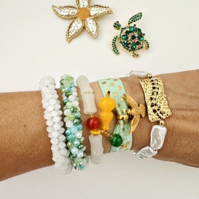 Pulseira e brincos coloridos com pedras e detalhes em dourado sendo usados no pulso.
