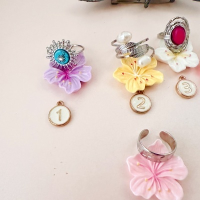 Anéis prateados com pedras e pérolas sobre flores artificiais com etiquetas numeradas