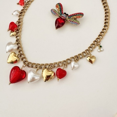 Colar dourado com pendentes de corações vermelhos, brancos e dourados e broche colorida em forma de inseto.