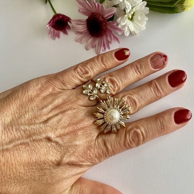 Mão com unhas vermelhas e anéis com pedras ao lado de flores coloridas