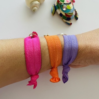 Pulseiras coloridas de tecido num braço com concha e tartaruga decorativa ao fundo