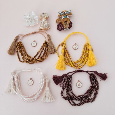 Pulseiras com contas e franjas coloridas numeradas de 1 a 4 com três broches decorativos acima.