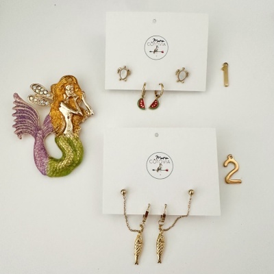 Brincos dourados em cartolina com logótipo Marta COTOVIA, sereia decorativa e números metálicos 1 e 2