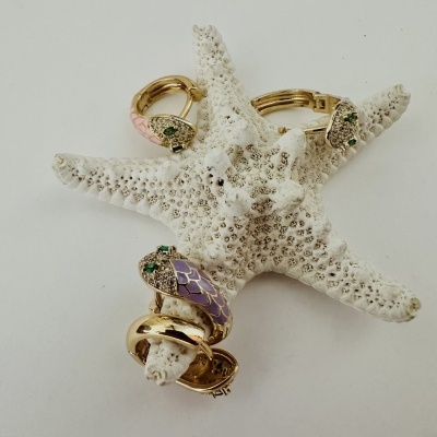 Joias douradas com pedras verdes e detalhes em esmalte rosa e lilás sobre estrela-do-mar branca.