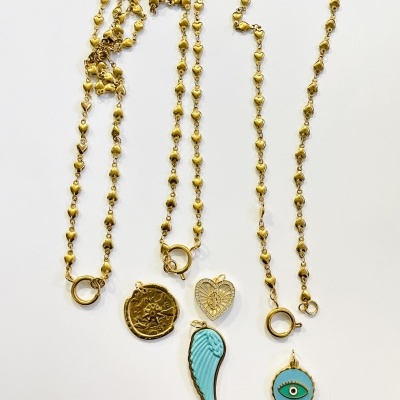 Três colares dourados com pingentes variados sobre fundo branco.