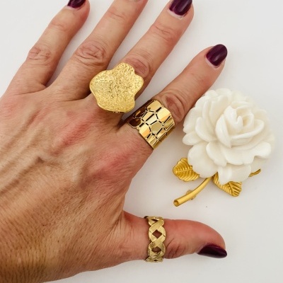 Mão com anéis dourados e unha pintada em fundo branco com flor de broche