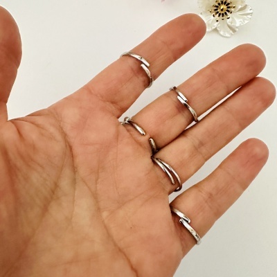 Mão com anéis prateados finos e flor decorativa ao fundo