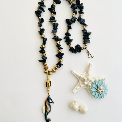 Colar com pedras pretas e douradas, cavalo-marinho pendente, estrela-do-mar, conchas e flor azul decorativa.