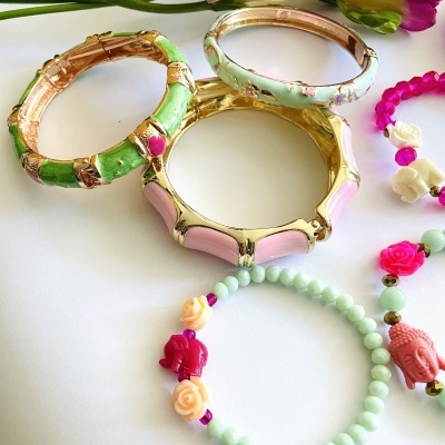 Pulseiras esmaltadas e de contas coloridas sobre superfície branca com flores ao fundo