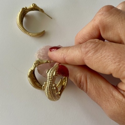 Brincos de argola dourados com textura escamada e mão segurando um deles