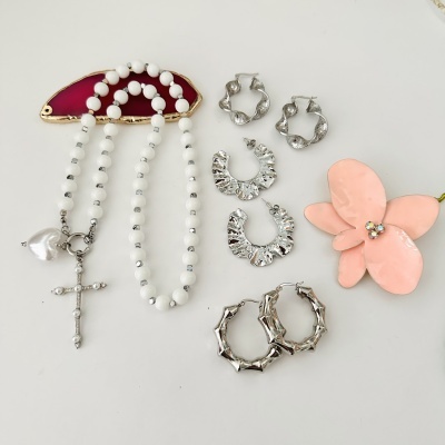 Colar de contas brancas com cruz e coração pendentes, três pares de brincos prateados e flor decorativa rosa