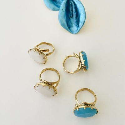 Anéis dourados com pedras azul claro e brancas sobre fundo branco com flores azuis decorativas