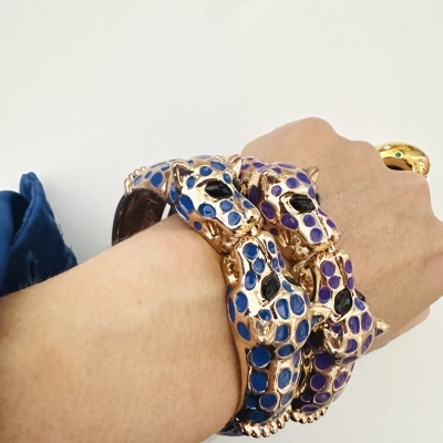 Bracelete dourado com cabeças de pantera azul e roxa num pulso humano
