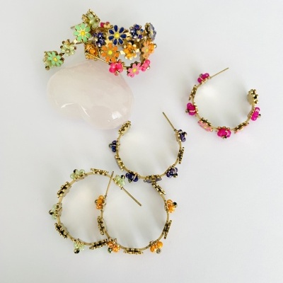 Brincos de argola dourados com flores coloridas sobre pedra branca