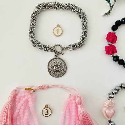 Pulseiras prateada com pingente de olho e rosa com contas e franjas sobre fundo claro