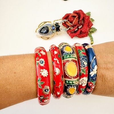 Pulseiras coloridas de tecido com padrões florais num pulso, broche de insecto e rosa vermelha em fundo branco