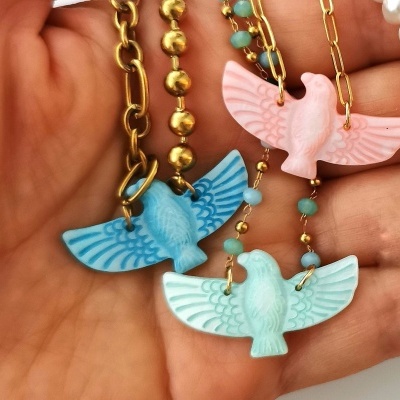 Três colares com pingentes de pássaros coloridos e correntes douradas na mão