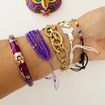 Braço com cinco pulseiras variadas e máscara decorativa ao fundo