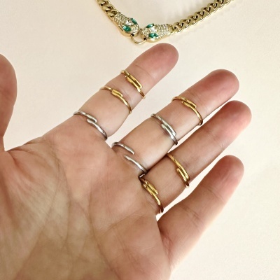 Anéis finos dourados e prateados na mão com corrente dourada e fecho de cabeças de serpente ao fundo