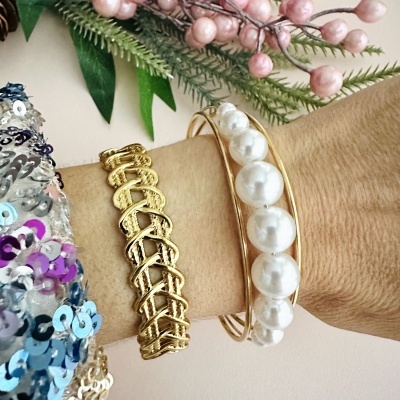 Braceletes dourados e pérolas no pulso com fundo floral