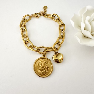 Pulseira dourada com pendentes redondo e coração sobre fundo branco próximo a flor branca