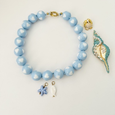 Colar azul com corações brancos e pendente decorativo, com pequenos adornos em fundo branco.