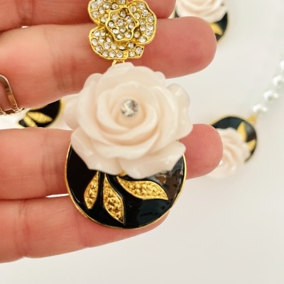 Brinco com flor branca, base dourada com pedras e disco preto com folhas douradas.