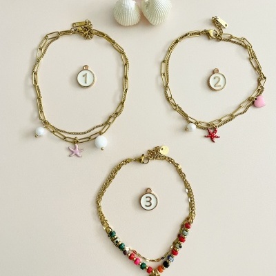 Três pulseiras douradas com pendentes coloridos, conchas brancas e flor cor-de-rosa num fundo branco