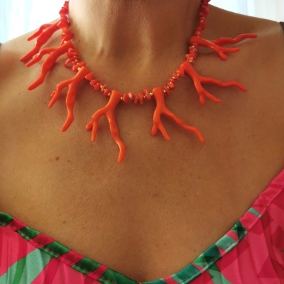 Colar de ramos de coral vermelho no pescoço de pessoa vestindo roupa rosa com padrão verde