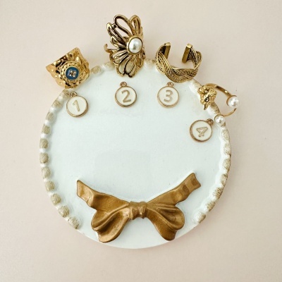 Conjunto de quatro anéis dourados numerados em suporte branco com laço dourado