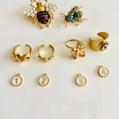 Anéis e broches decorativos com abelhas, pérolas e medalhas numeradas