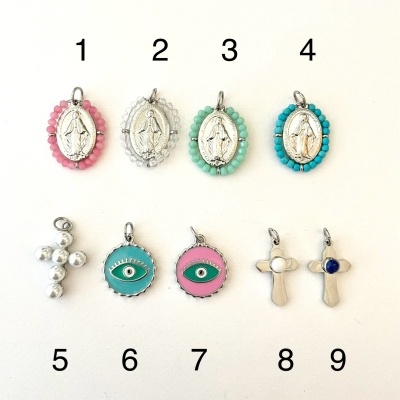 Nove pendentes variados com medalhas, olhos decorativos e cruzes em metal e cores distintas