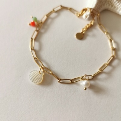 Pulseira dourada com pendentes de concha, pérola e contas coloridas sobre fundo claro.